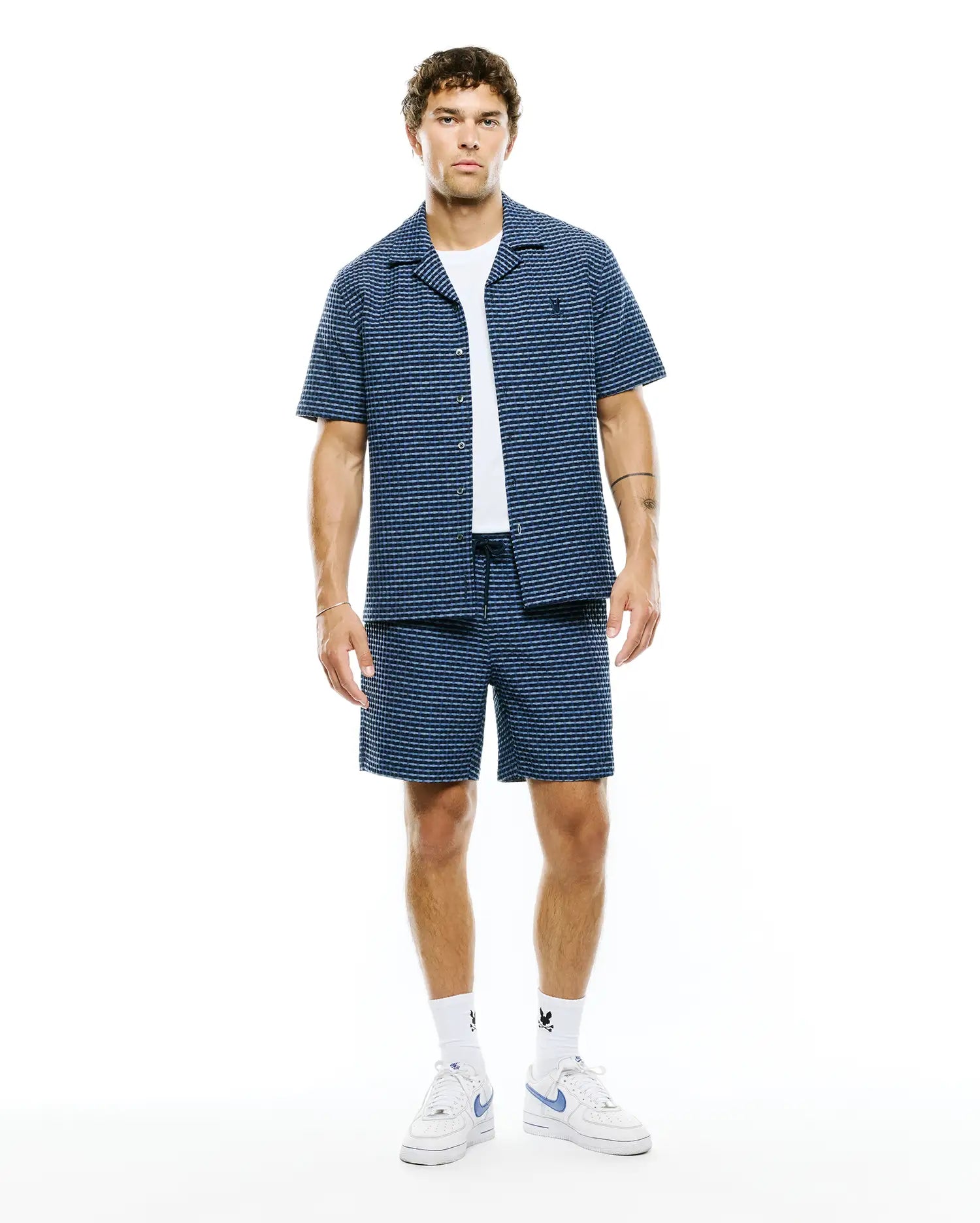 Mens Erik Raised Check Shirt and matching shorts, a relaxed navy blue set with light blue raised check stripes, featuring an open collar shirt with a small embroidered Psycho Bunny skull logo on the left chest.