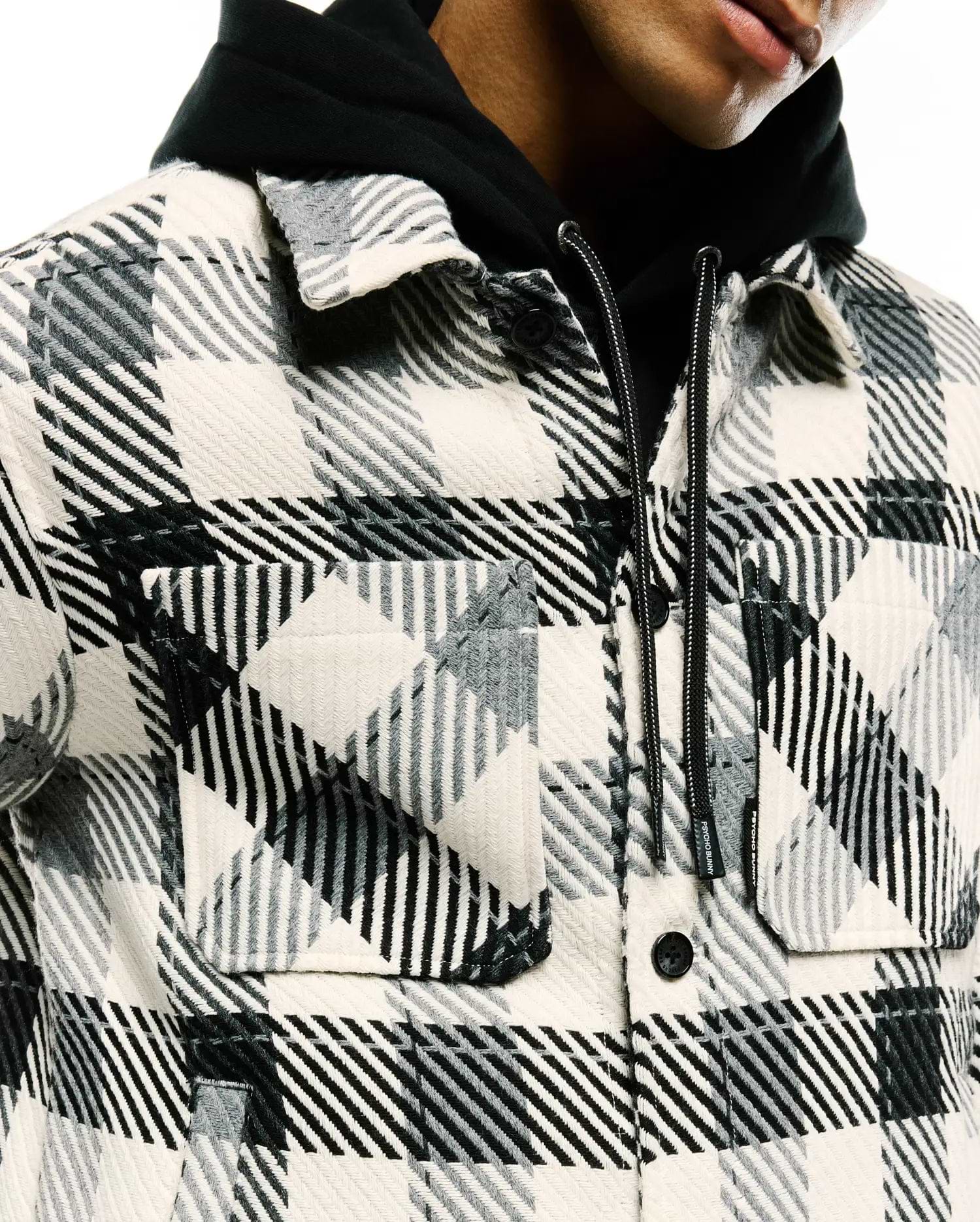 Mens Kessler Relaxed Plaid Overshirt in cream, black, and grey, featuring a relaxed fit, textured woven plaid fabric, two button-flap chest pockets, and a small Psycho Bunny tag on the layered hoodie's drawstring.