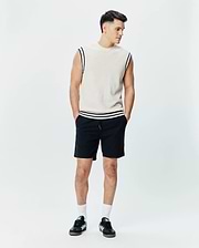 Mens Peter Knit Vest in cream, featuring a classic fit, fine knit texture, navy and white striped armhole and hem trim, and a small embroidered Psycho Bunny skull on the left chest, paired with black drawstring shorts.