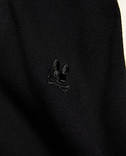 Mens Rafferty Cardigan in black fine knit fabric with a subtle ribbed texture, featuring a small, tonal black embroidered Psycho Bunny skull logo and a cream side stripe.