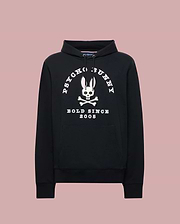 The Psycho Bunny MENS ARCHIVE HOODIE (MT0500009) is a black cotton knit pullover with a front pocket, showcasing an archive-inspired white Bunny skull and crossbones and "PSYCHO BUNNY BOLD SINCE 2005" over a light pink backdrop.