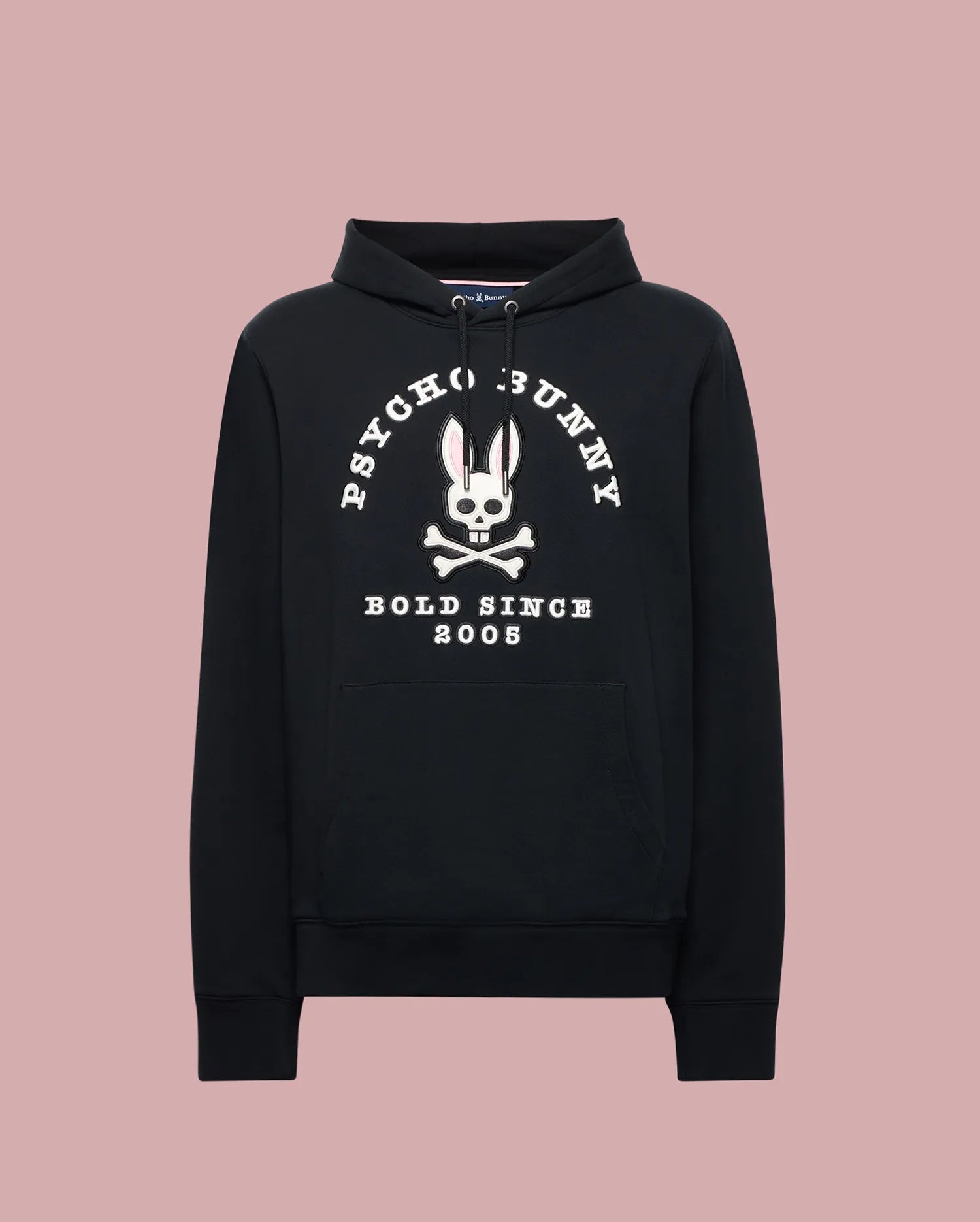 The Psycho Bunny MENS ARCHIVE HOODIE (MT0500009) is a black cotton knit pullover with a front pocket, showcasing an archive-inspired white Bunny skull and crossbones and "PSYCHO BUNNY BOLD SINCE 2005" over a light pink backdrop.
