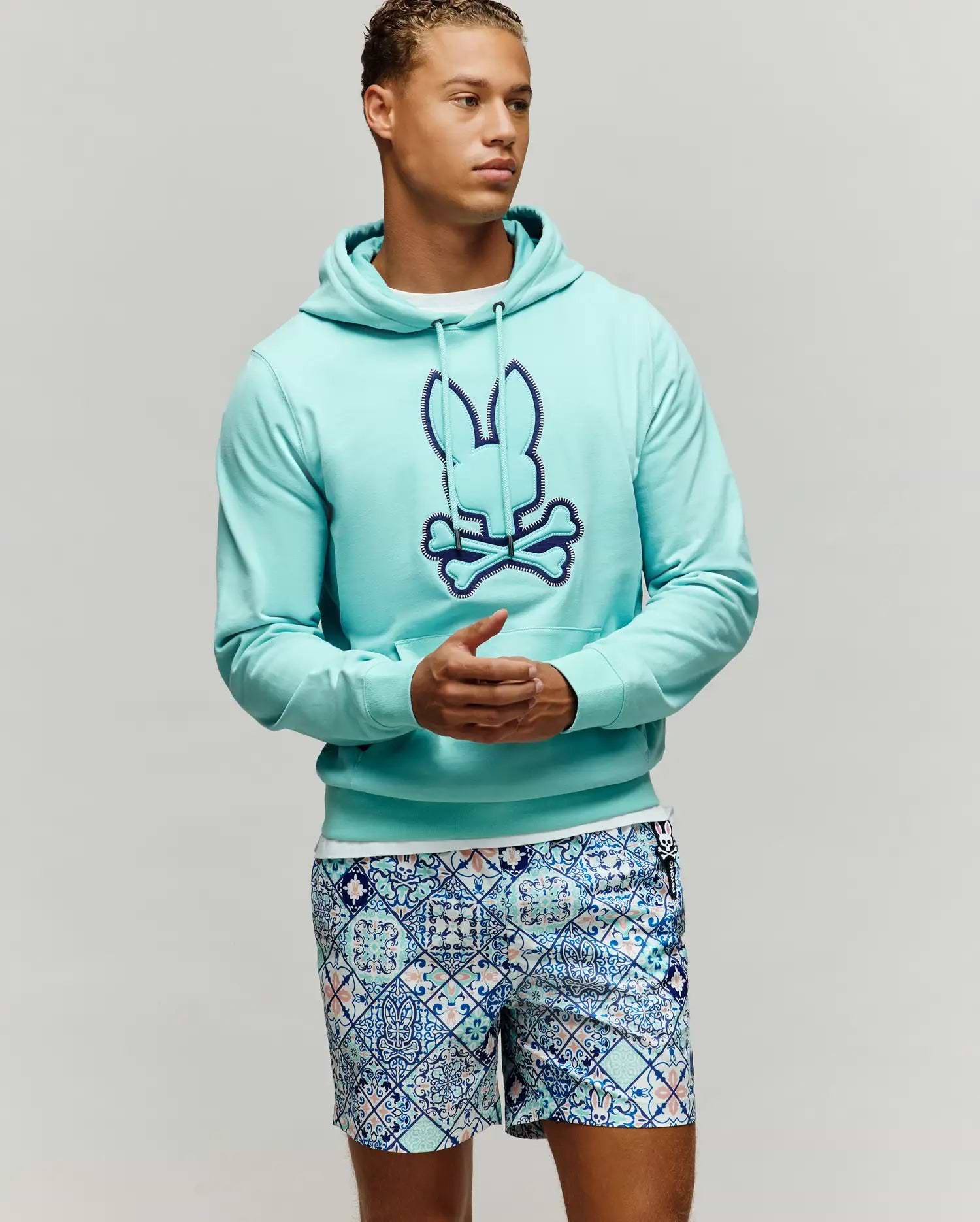 Mens Gage Patch Hoodie, an aqua French terry classic fit hoodie with a large embroidered dark blue and light blue Psycho Bunny skull logo on the chest, featuring a drawstring hood and kangaroo pocket.