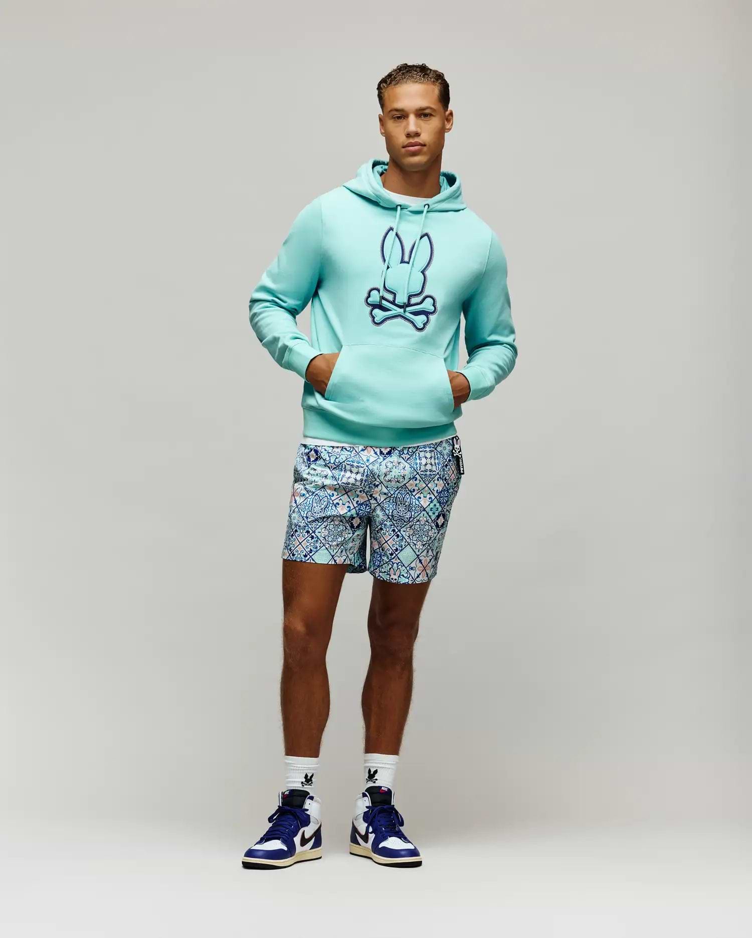 Aqua French terry Mens Gage Patch Hoodie, classic fit, with a large embroidered dark blue Psycho Bunny skull logo on the chest, paired with patterned blue and white shorts and white logo socks.