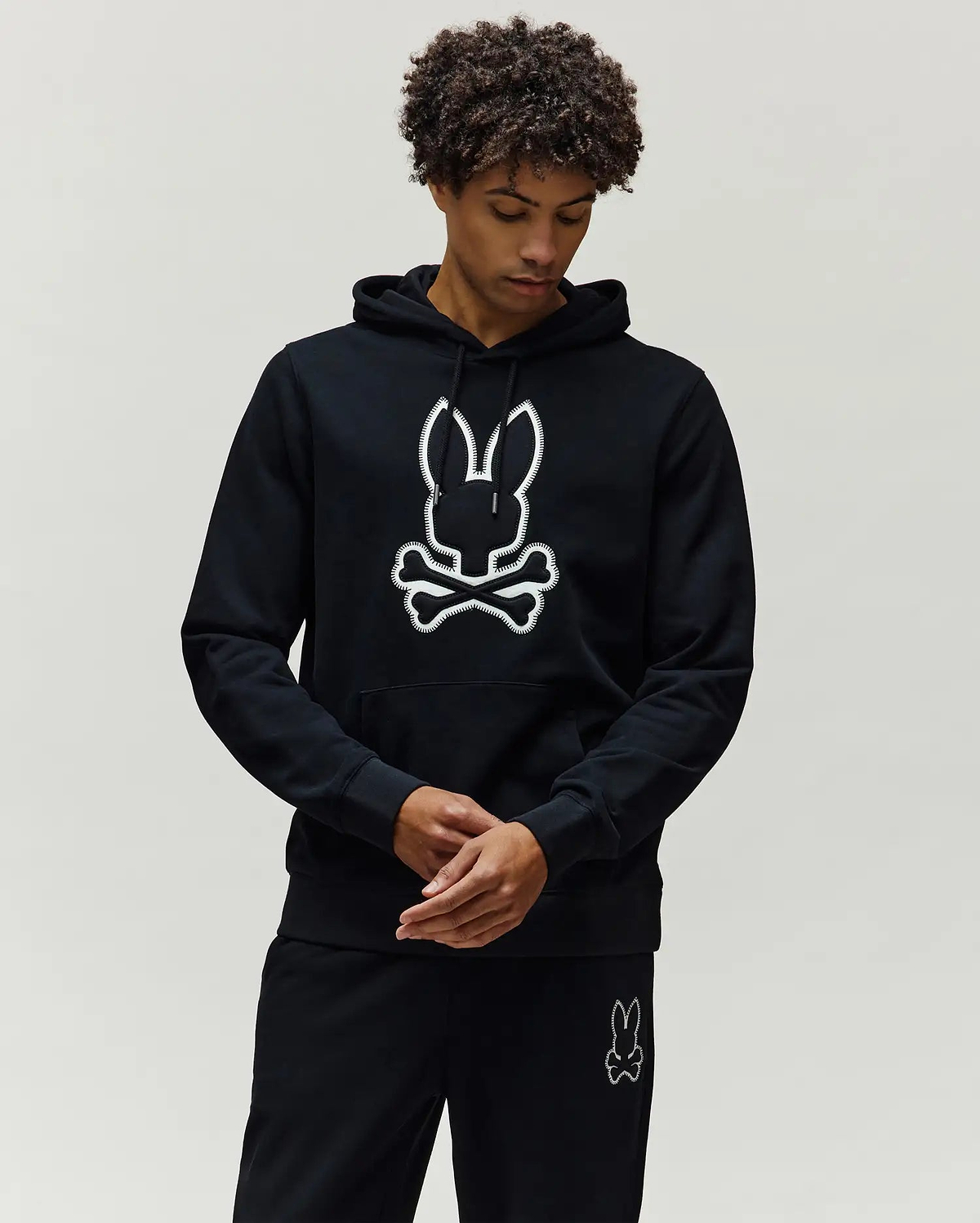Mens Gage Patch Hoodie, black classic fit with a drawstring hood and kangaroo pocket, featuring a large white embroidered Psycho Bunny skull logo with a stitched outline on the chest.