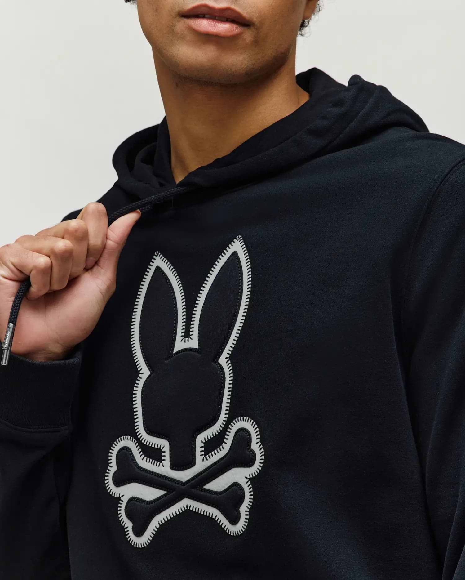 Mens Gage Patch Hoodie, black classic fit hoodie in soft jersey knit, featuring a large central white Psycho Bunny skull logo patch with detailed stitching and branded drawstring aglets.