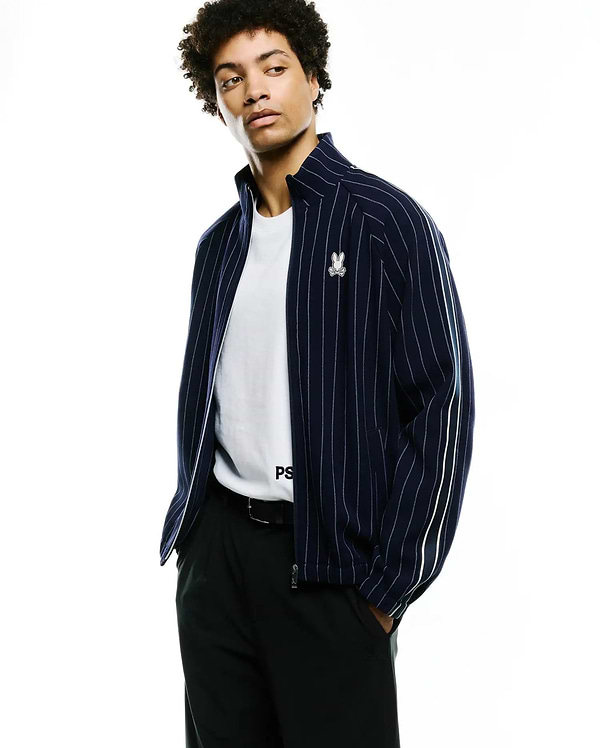 Mens Harland Double Weave Chalk Stripe Track Jacket, navy blue with white vertical chalk stripes, full zip, small embroidered Psycho Bunny skull logo on left chest, and white double stripes on sleeves. (1)
