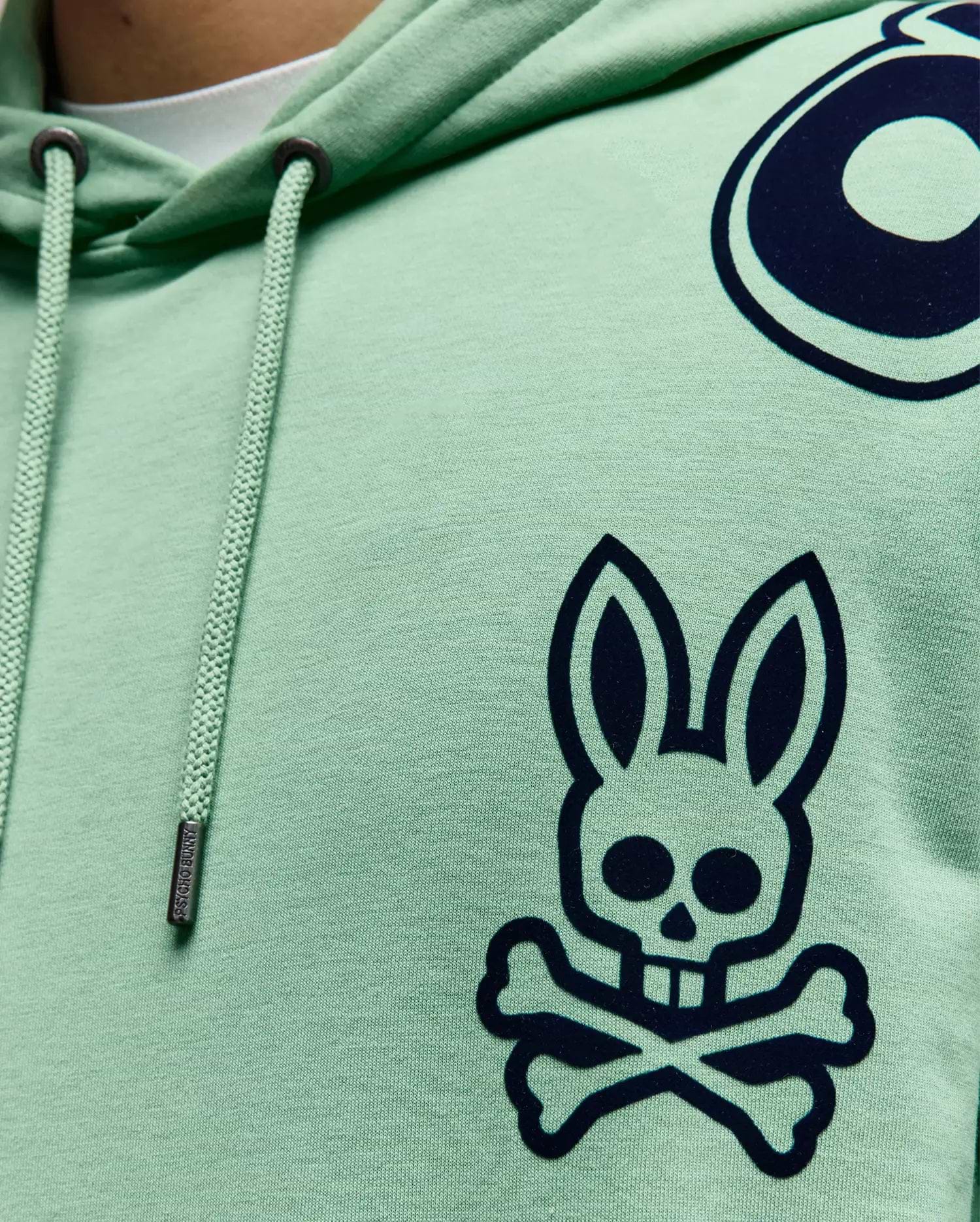 Mens Toby Oversized Hoodie in mint green jersey, featuring a large navy Psycho Bunny skull logo on the chest, partial circular graphic, and branded drawstrings with metal tips.