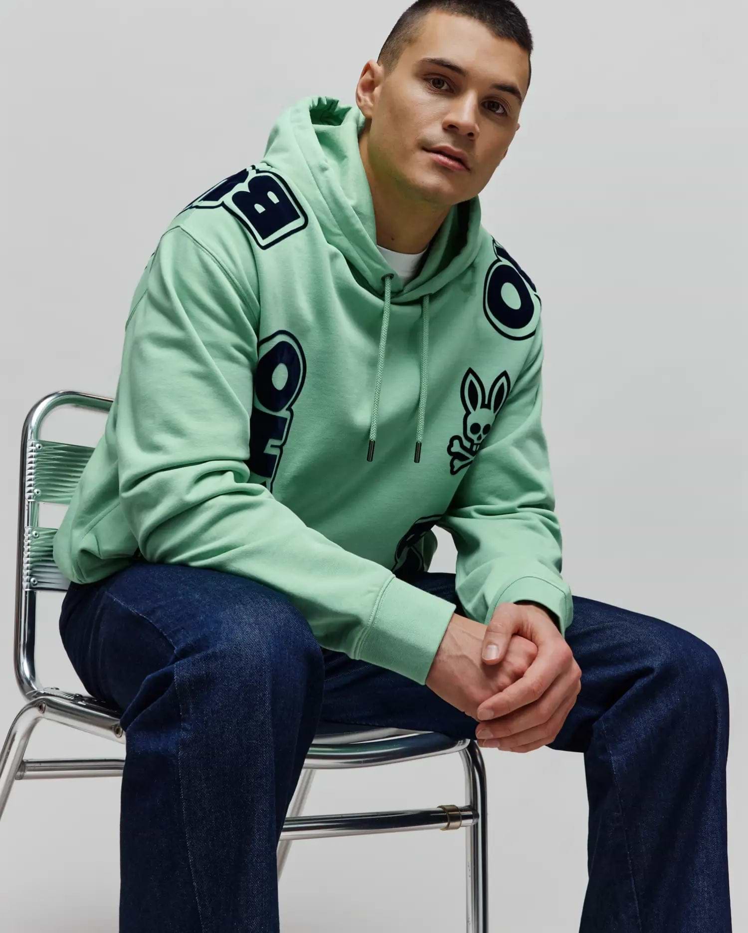 Mens Toby Oversized Hoodie in mint green, crafted from soft jersey, featuring bold dark blue Psycho Bunny lettering across the shoulders and a small bunny skull logo on the left chest.