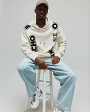 Mens Toby Oversized Hoodie in cream, featuring bold black scattered PSYCHO BUNNY lettering and a prominent bunny skull logo on the left chest, made from soft fleece.