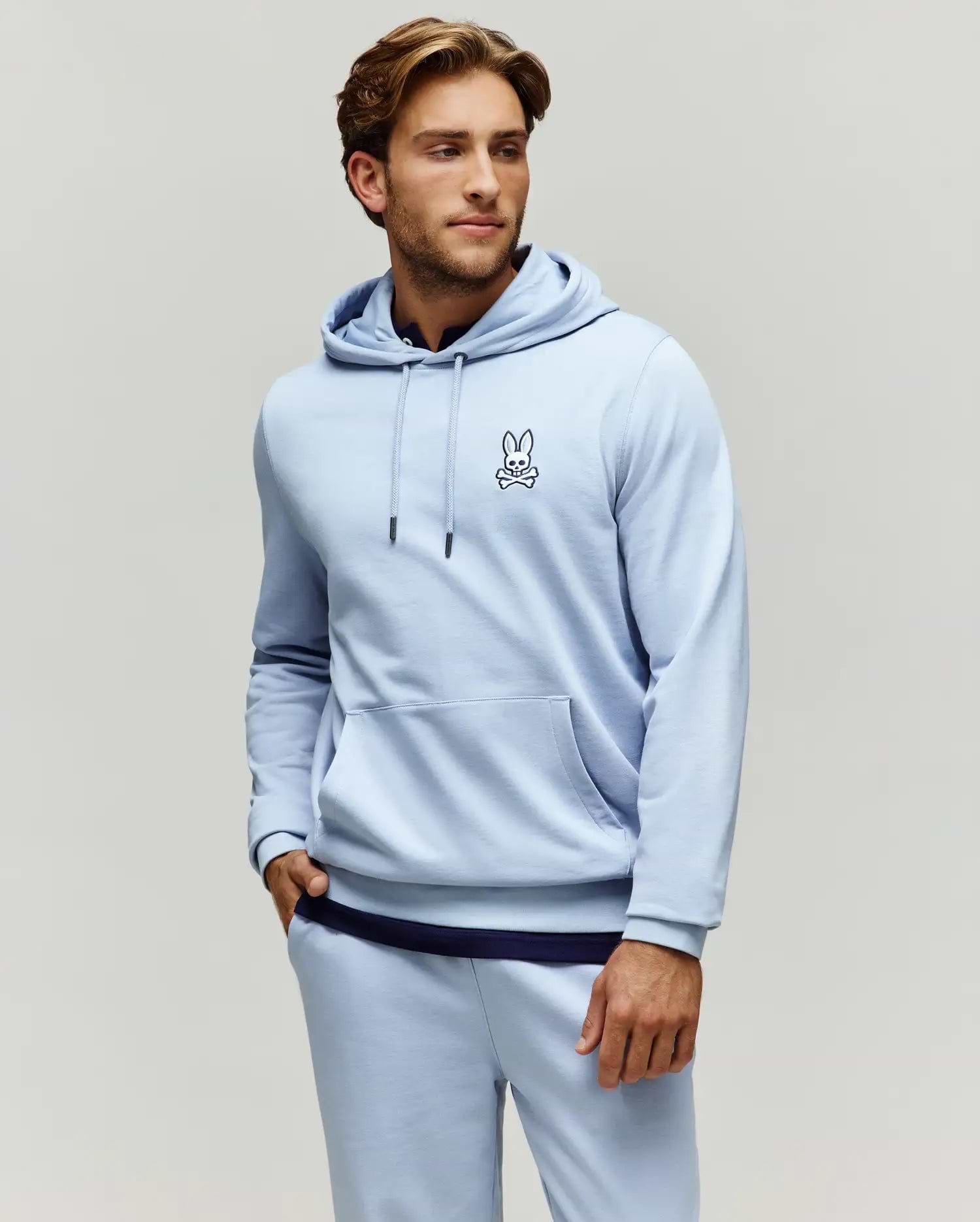 Mens Timothy 4k Bunny Hoodie, a light blue classic fit jersey hoodie with a kangaroo pocket, black drawstrings, and a small embroidered Psycho Bunny skull logo on the left chest.