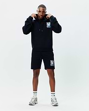 Black Mens Isaac Print Hoodie and matching shorts, featuring a vibrant, abstract Psycho Bunny skull graphic on the left chest and left thigh. Relaxed fit, soft french terry hoodie with drawstring, jersey shorts.
