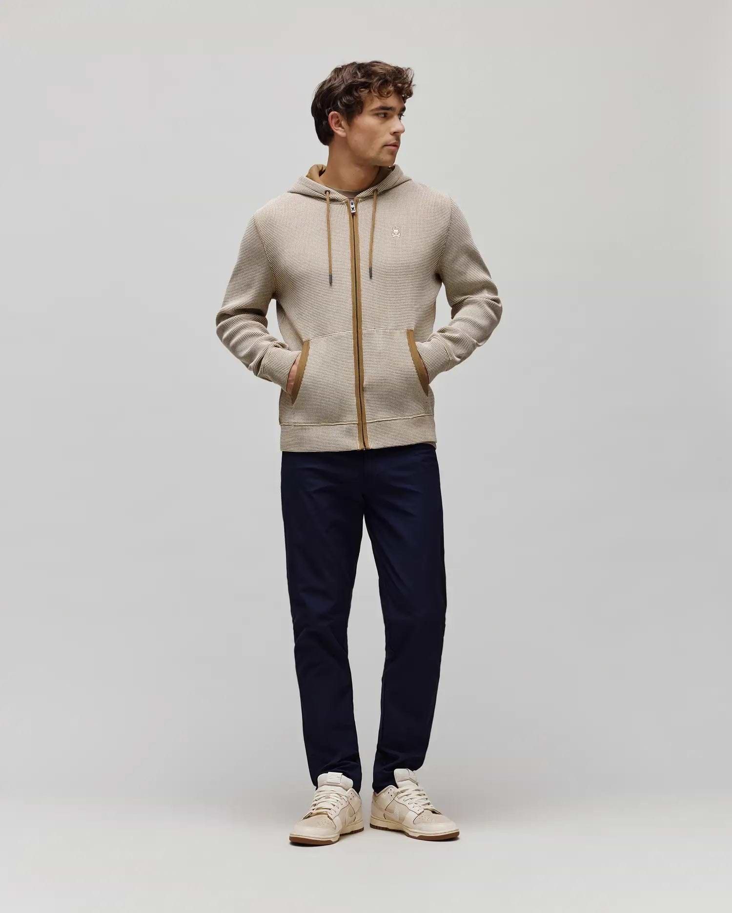 Mens Maxton Waffle Full Zip Hoodie in beige waffle knit with a subtle brown pattern, featuring a brown full zip, hood lining, and pocket trim, with a small embroidered Psycho Bunny skull logo on the left chest.