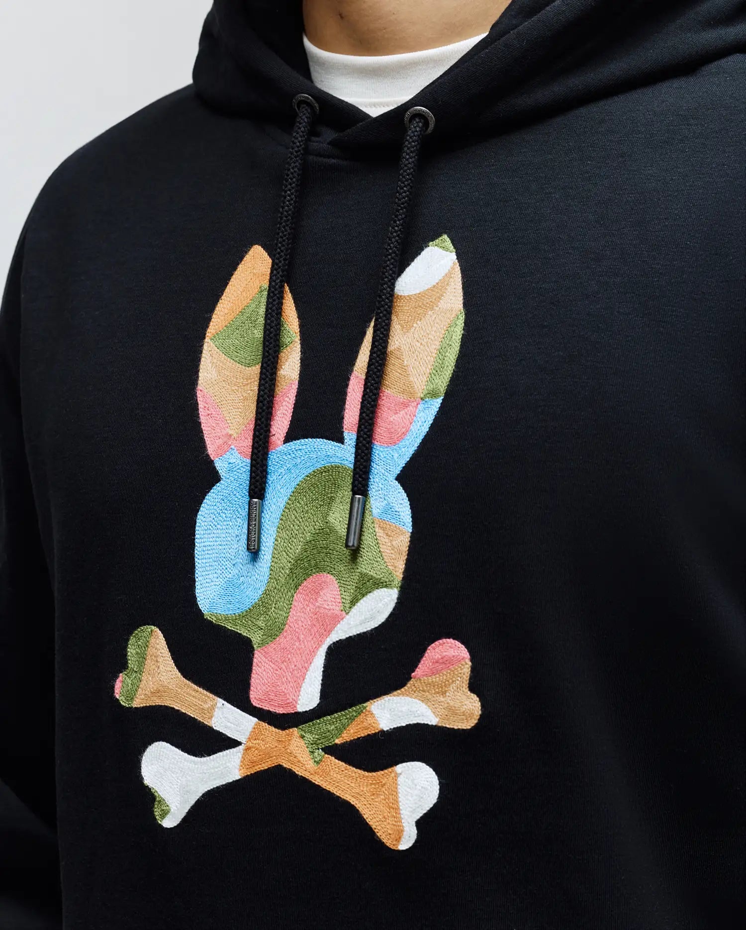 MENS ARA HOODIE, a black classic fit French terry hoodie with a large, central, multi-colored embroidered Psycho Bunny skull logo in blue, green, pink, orange, and white, featuring branded drawstring tips.