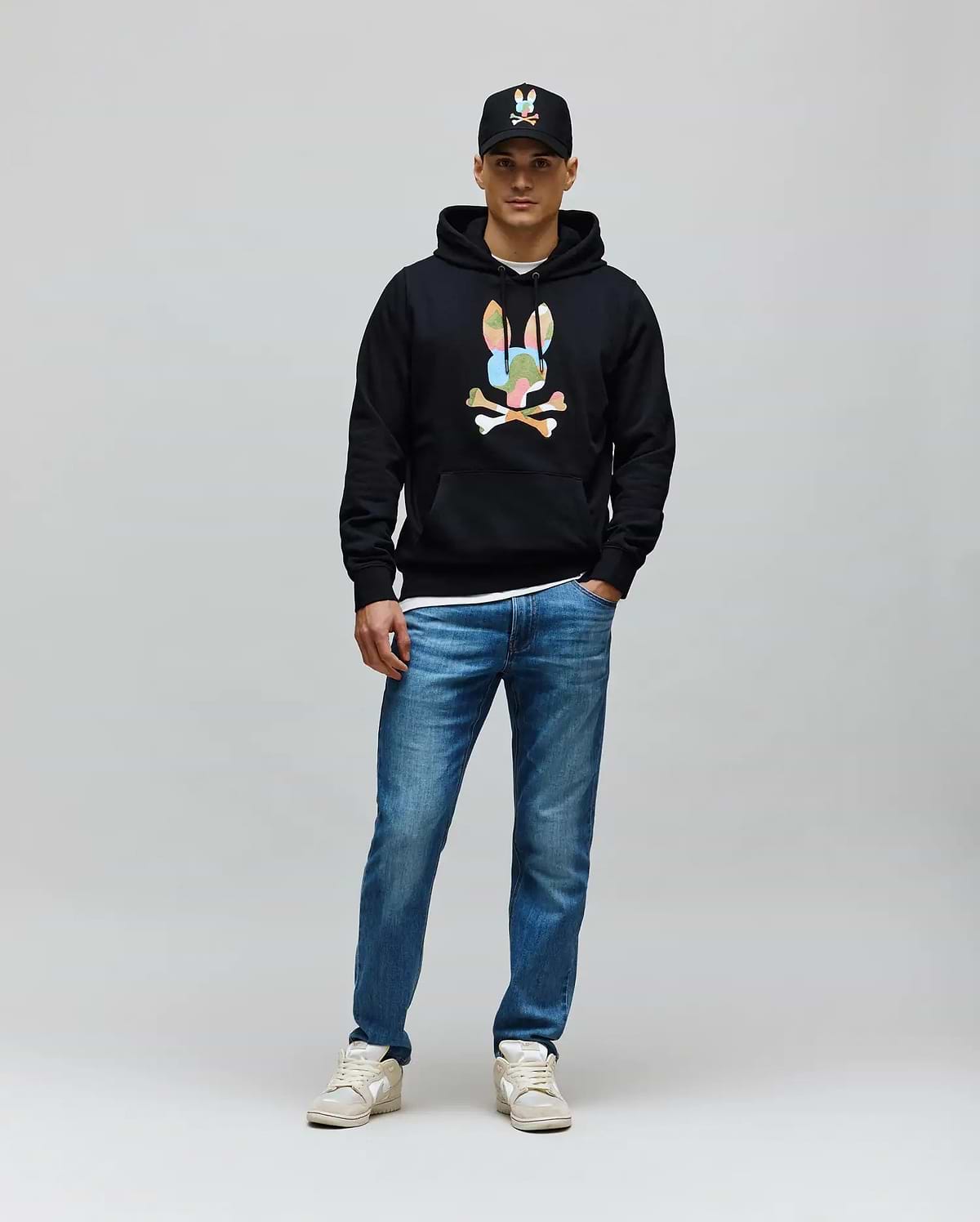 Mens Ara Hoodie, a black classic fit French terry hoodie featuring a large, colorful camouflage Psycho Bunny skull logo with white crossbones on the chest, plus a front pouch pocket and drawstring hood.