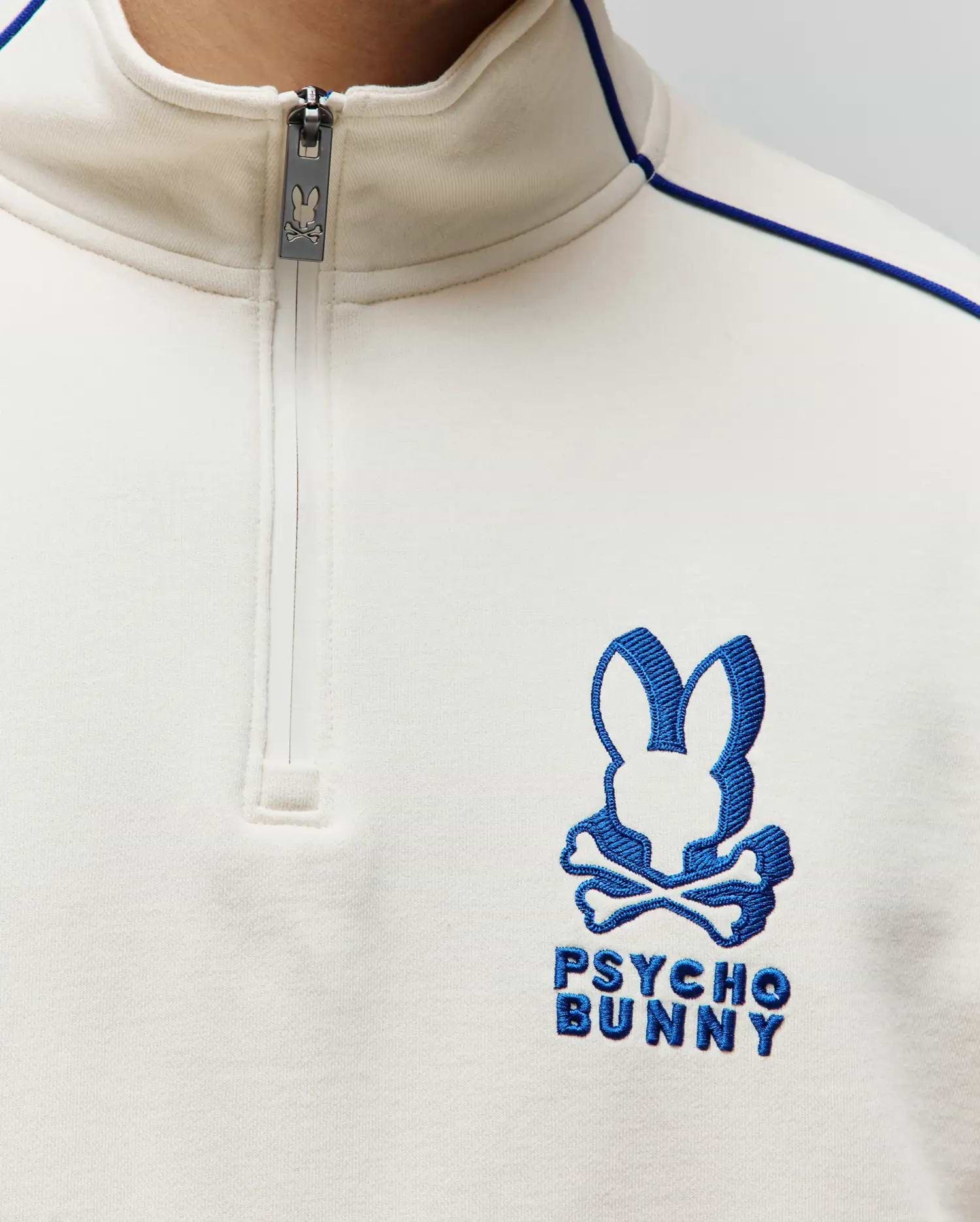 Mens Toby 1/4 Zip in cream smooth knit, featuring a royal blue embroidered Psycho Bunny skull logo on the left chest, blue piping detail, and a branded zipper pull.