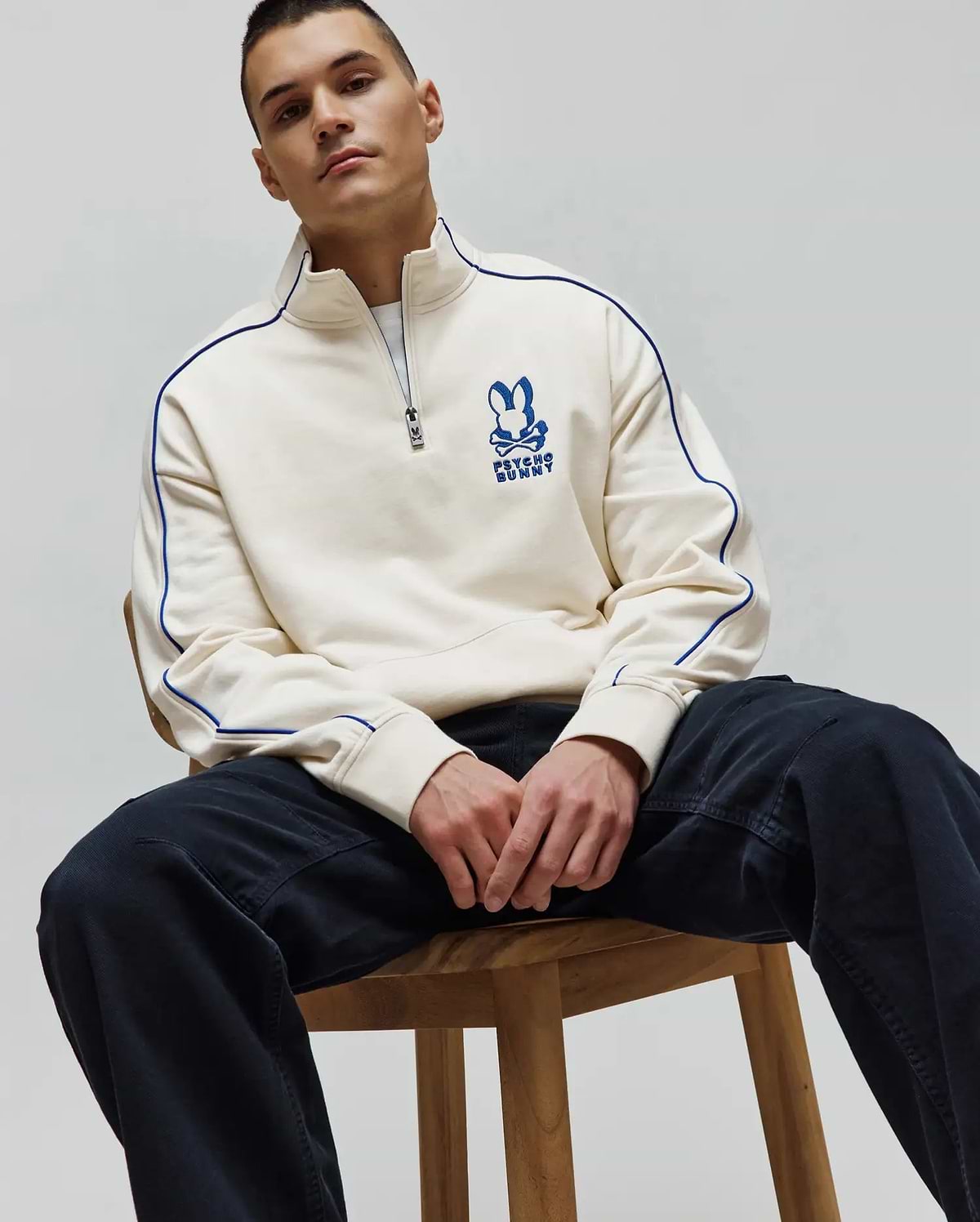 Mens Toby 1/4 Zip, a cream relaxed fit French terry sweatshirt with royal blue piping on sleeves and collar, featuring an embroidered royal blue Psycho Bunny skull logo on the left chest and a branded zipper pull.