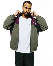Mens Alder Nylon Colorblock Jacket: Relaxed fit olive green, purple, and black crinkled nylon full-zip jacket featuring a colorblock design, elastic cuffs, and Psycho Bunny text on the chest.