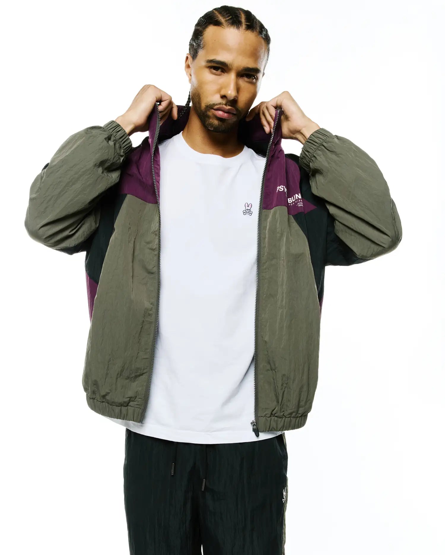 Mens Alder Nylon Colorblock Jacket: Relaxed fit olive green, purple, and black crinkled nylon full-zip jacket featuring a colorblock design, elastic cuffs, and Psycho Bunny text on the chest.