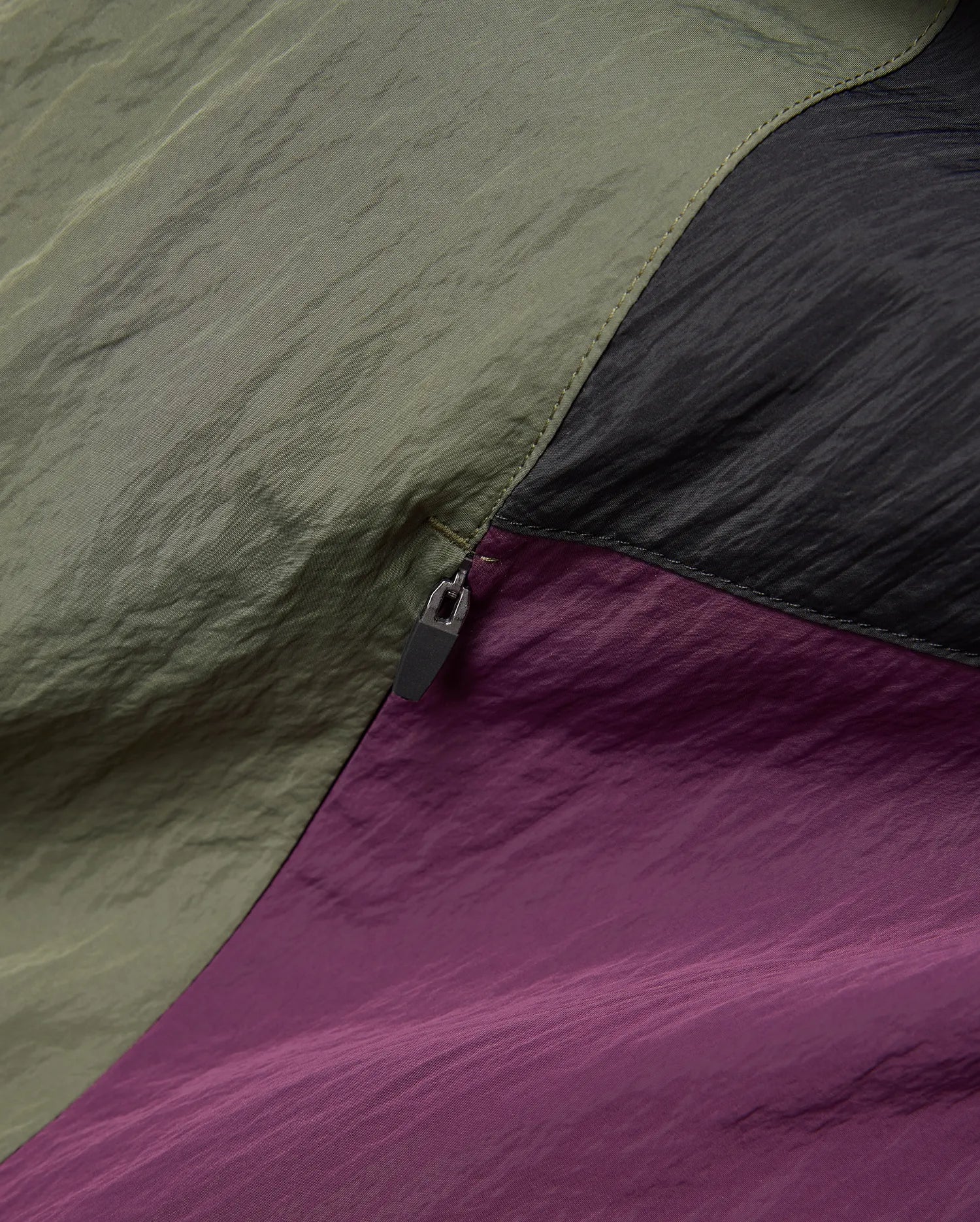 Mens Alder Nylon Colorblock Jacket in a premium crinkled nylon fabric, showcasing bold panels of olive green, deep black, and rich plum, accented by precise stitching and a sleek zipper pull.