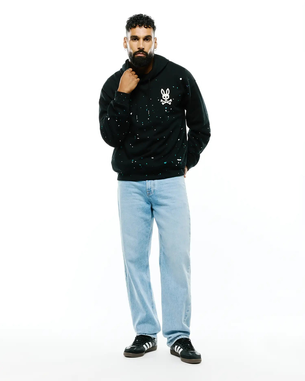 Mens Malcom Splatter Hoodie, a black relaxed fit French terry hoodie featuring an all-over white and teal splatter print and a small embroidered white Psycho Bunny skull logo on the left chest.