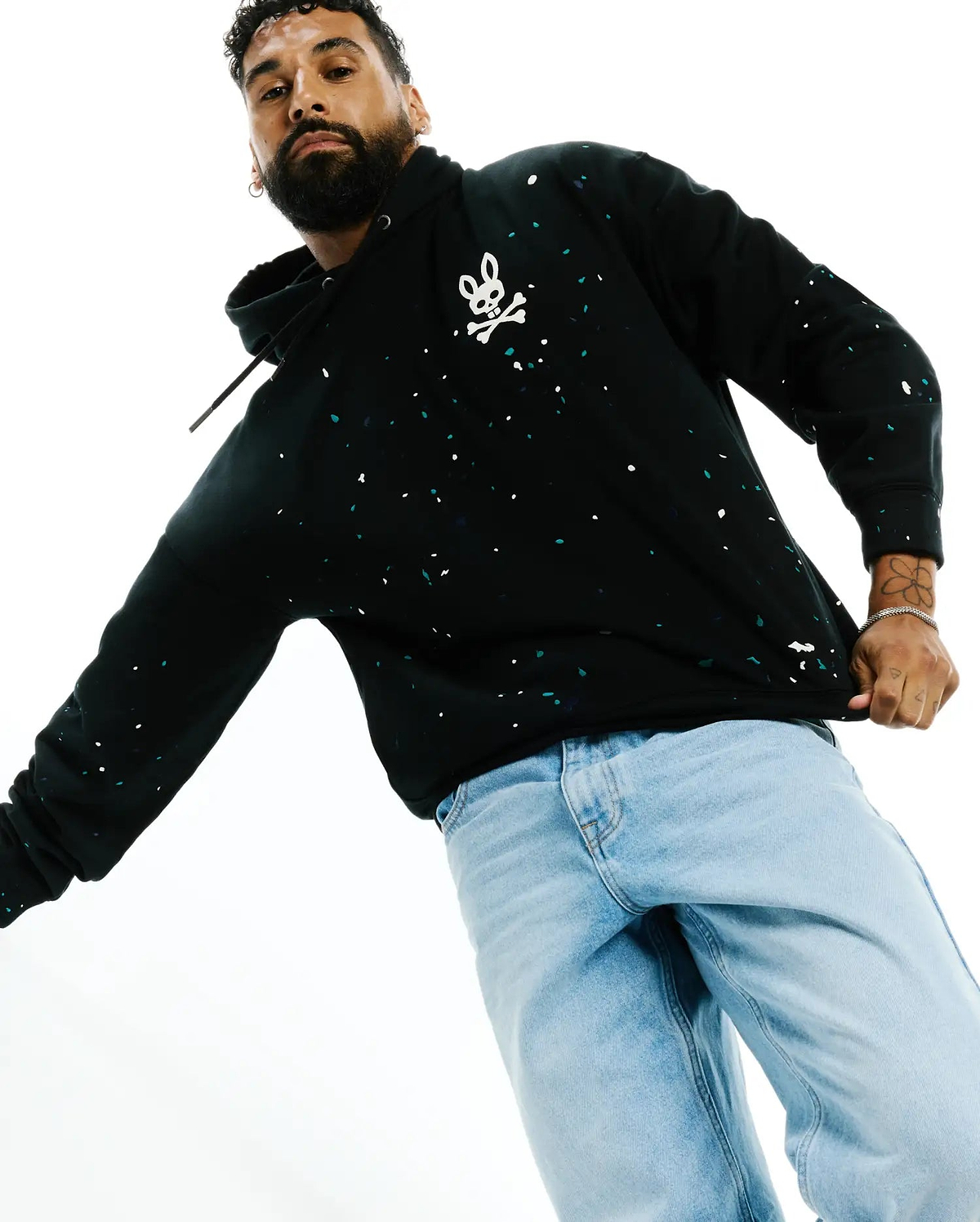 Mens Malcom Splatter Hoodie, a black relaxed fit French terry hoodie featuring a bold white and teal splatter print and a large white Psycho Bunny skull logo on the chest.
