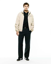Mens Alder Nylon Jacket in beige, featuring a relaxed fit, smooth nylon texture, full black zip, stand collar, and a small black PSYCHO BUNNY text logo embroidered on the left chest.