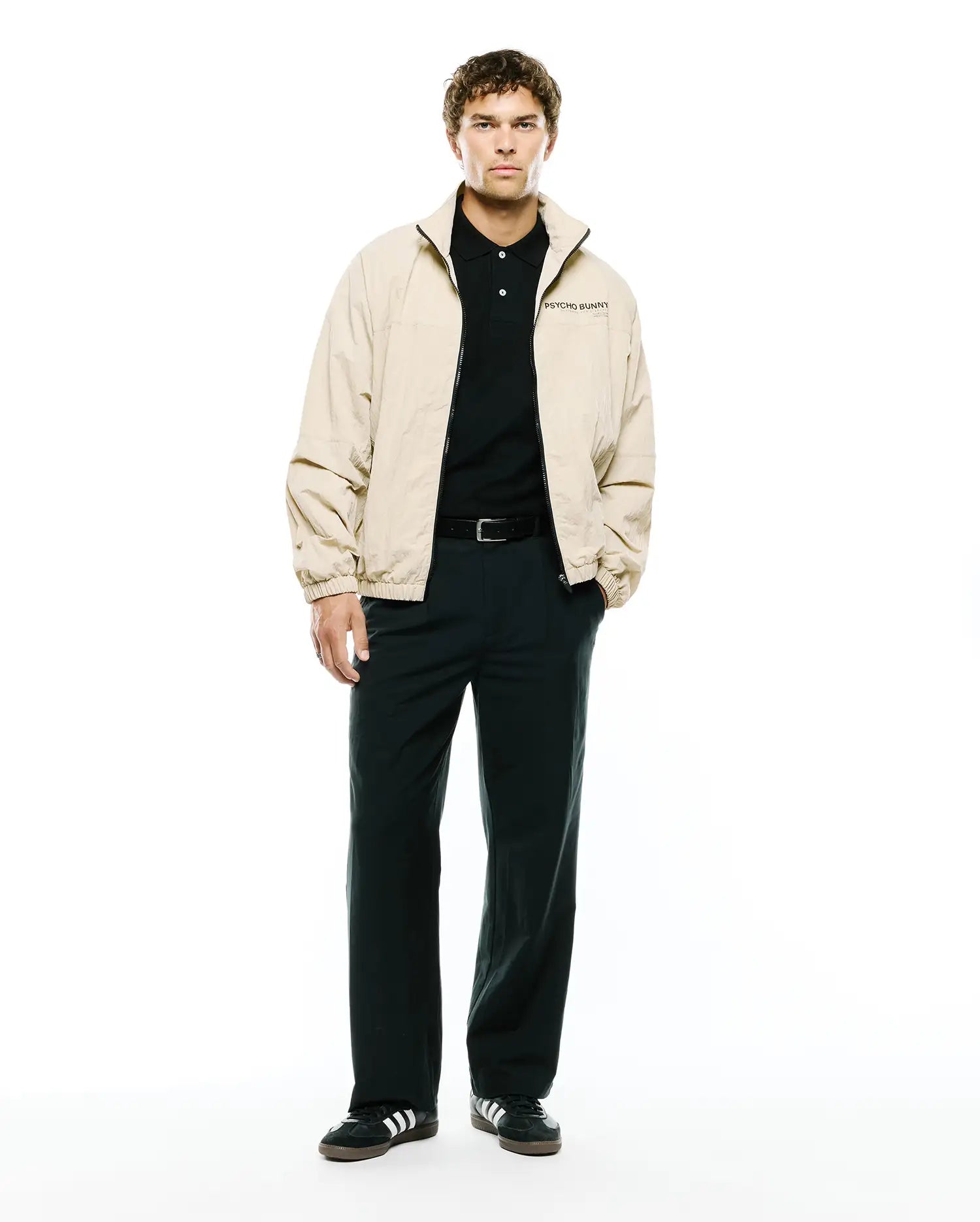 Mens Alder Nylon Jacket in beige, featuring a relaxed fit, smooth nylon texture, full black zip, stand collar, and a small black PSYCHO BUNNY text logo embroidered on the left chest.