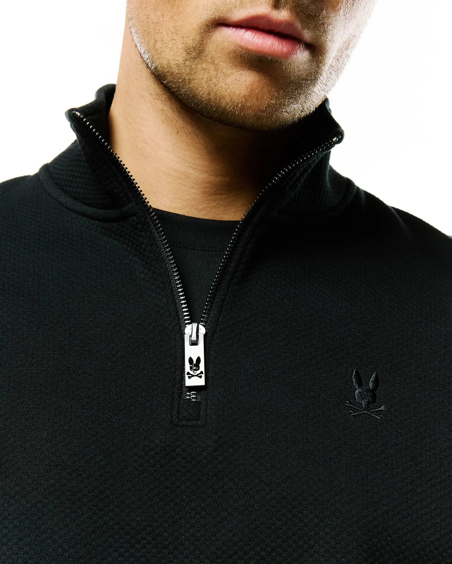 Mens Marc Textured 1/4 Zip in black, featuring a textured knit fabric, a 1/4 zip closure with a metallic Psycho Bunny logo zipper pull, and a small, tonal embroidered bunny skull on the left chest.