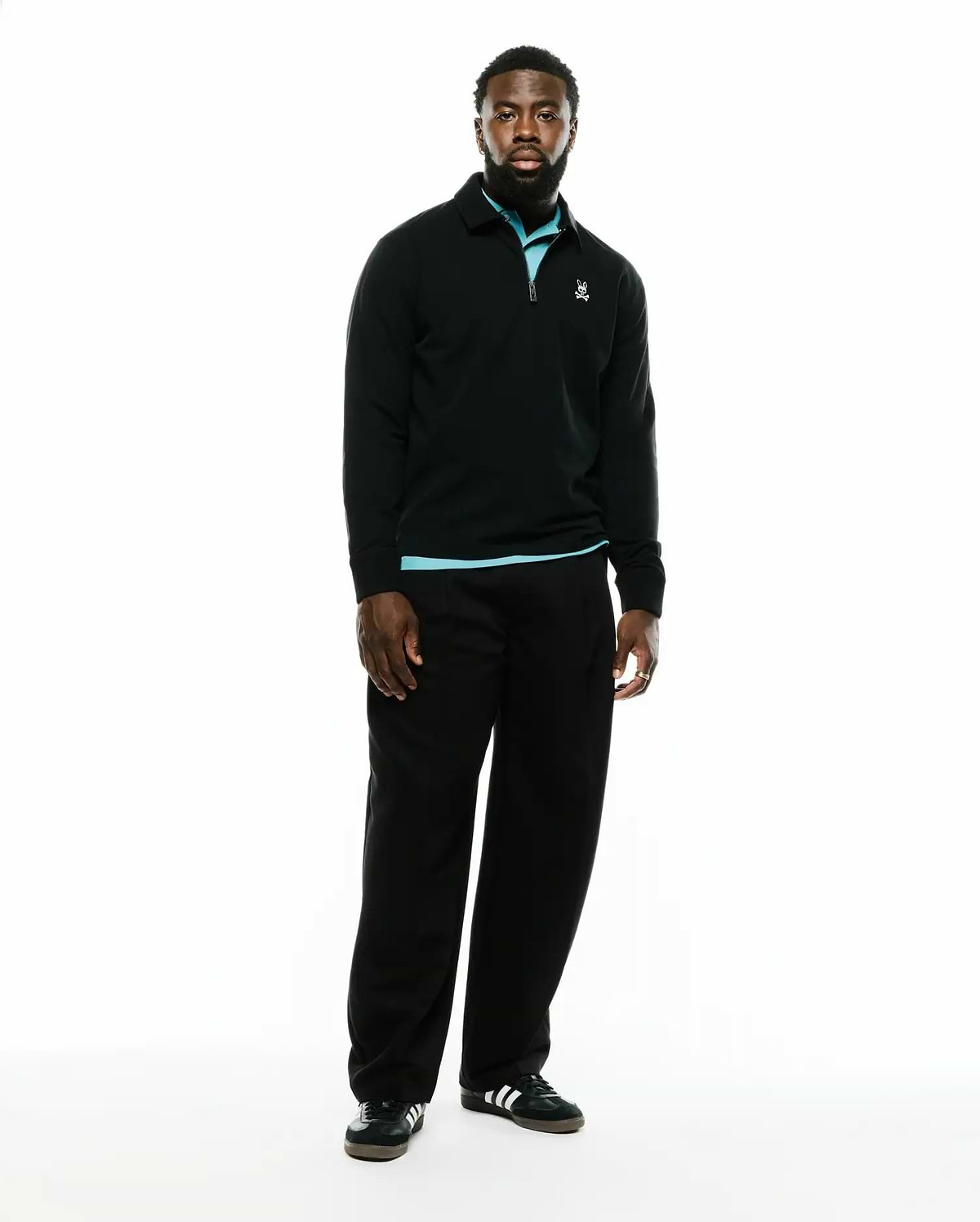 Men's Samson Quarter-Zip Sweater, a classic fit black smooth knit quarter-zip with a collared neckline, light blue accent at the collar and hem, and a small embroidered white Psycho Bunny skull logo on the left chest. (1)