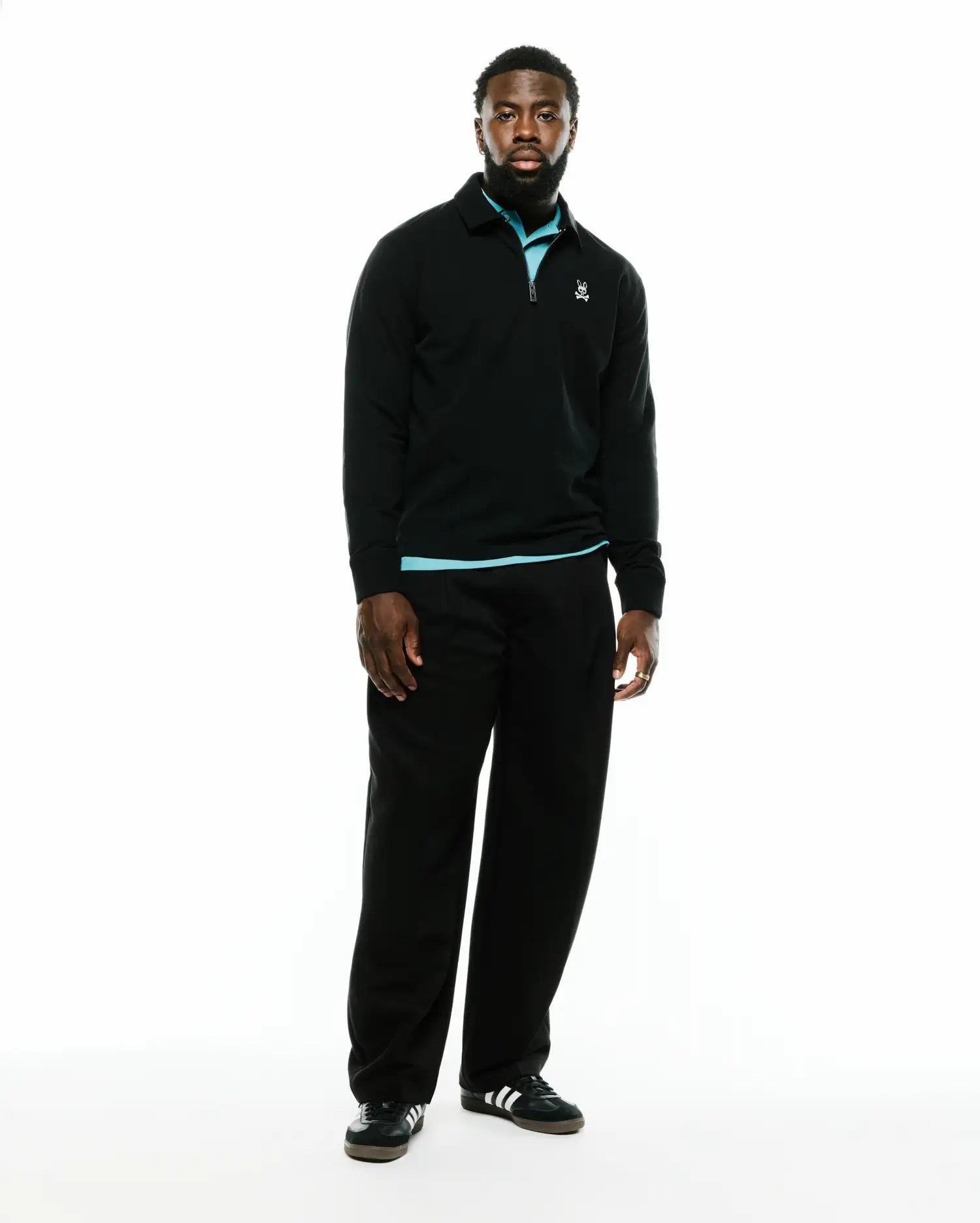 Men's Samson Quarter-Zip Sweater, a classic fit black smooth knit quarter-zip with a collared neckline, light blue accent at the collar and hem, and a small embroidered white Psycho Bunny skull logo on the left chest. (1)