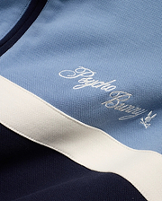 Men's Jacques Pique Track Jacket in light blue and navy pique fabric with a white stripe, featuring an embroidered white Psycho Bunny script logo and small bunny skull logo on the chest. (6)