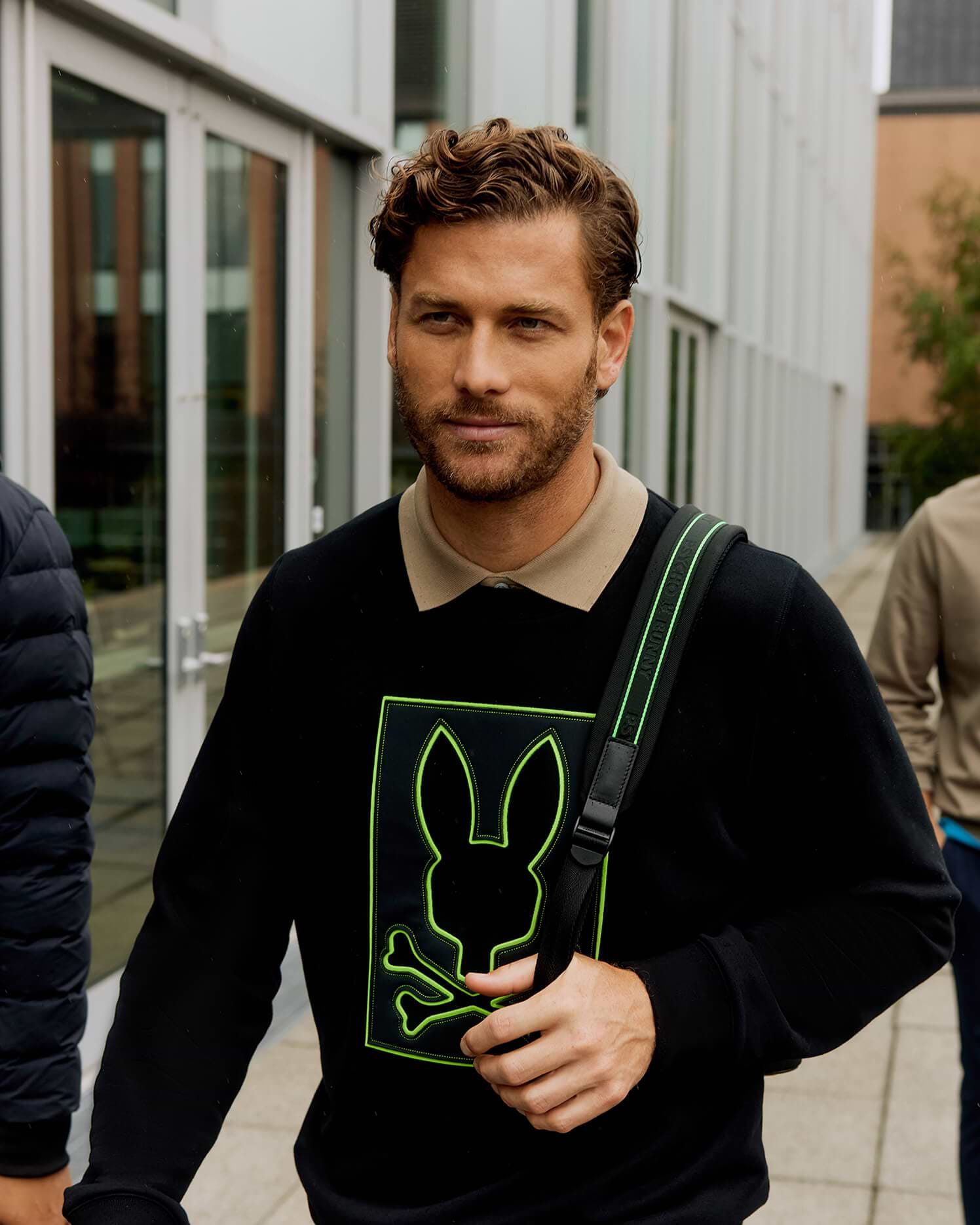 Mens Los Angeles Fleece Sweatshirt, black, featuring a large central neon green outlined Psycho Bunny skull logo with dotted texture, worn over a beige polo, in a classic fit soft fleece.