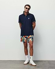 Navy pique polo with orange striped collar and cuffs, featuring a white embroidered Psycho Bunny logo on the chest, paired with vibrant Mens Wes All Over Print Swim Trunk shorts.