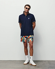 Navy pique polo with orange striped collar and cuffs, featuring a white embroidered Psycho Bunny logo on the chest, paired with vibrant Mens Wes All Over Print Swim Trunk shorts.