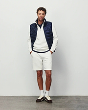 Mens Marc Textured Short in cream pique with a small embroidered Psycho Bunny logo on the left thigh, styled with a matching textured quarter-zip pullover featuring a chest logo and a navy quilted vest.
