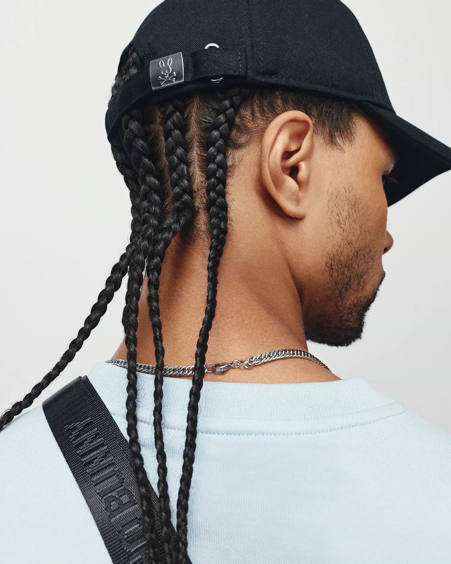 Mens Ambrose Baseball Cap, black cotton twill, featuring a silver Psycho Bunny skull logo on the adjustable back strap, paired with a light blue crewneck jersey top and a black strap embossed with Psycho Bunny text.