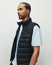 Mens Emerik Puffer Vest, a black quilted puffer with stand collar, full zip, and small embroidered Psycho Bunny skull logo on left chest, plus subtle text pattern on inner lining.