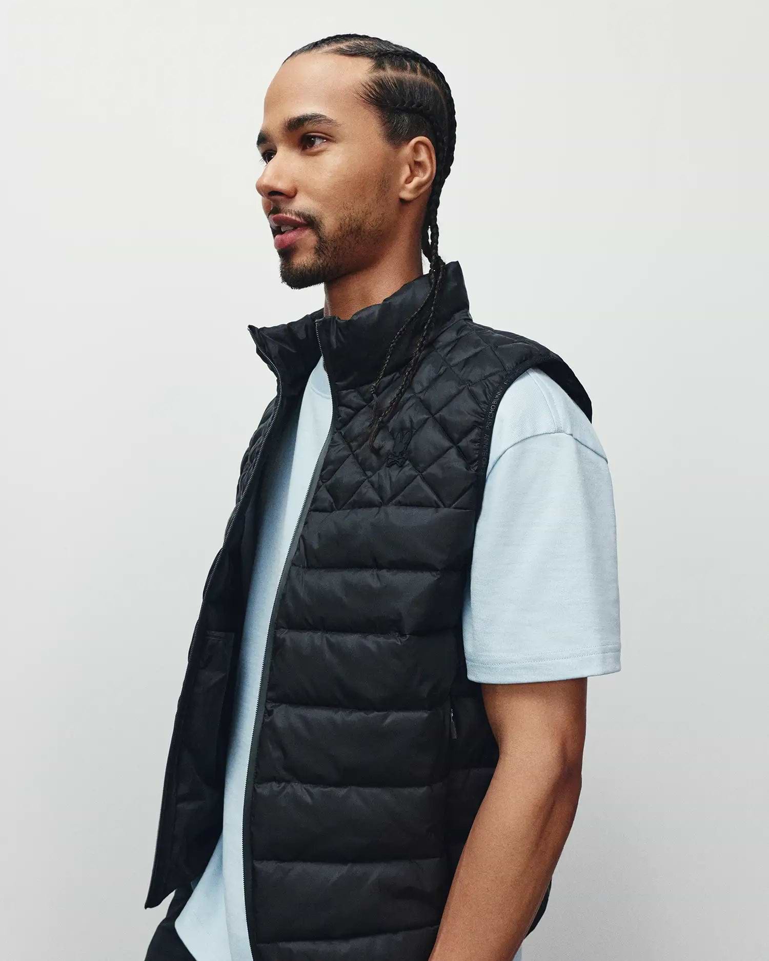 Mens Emerik Puffer Vest, a black quilted puffer with stand collar, full zip, and small embroidered Psycho Bunny skull logo on left chest, plus subtle text pattern on inner lining.