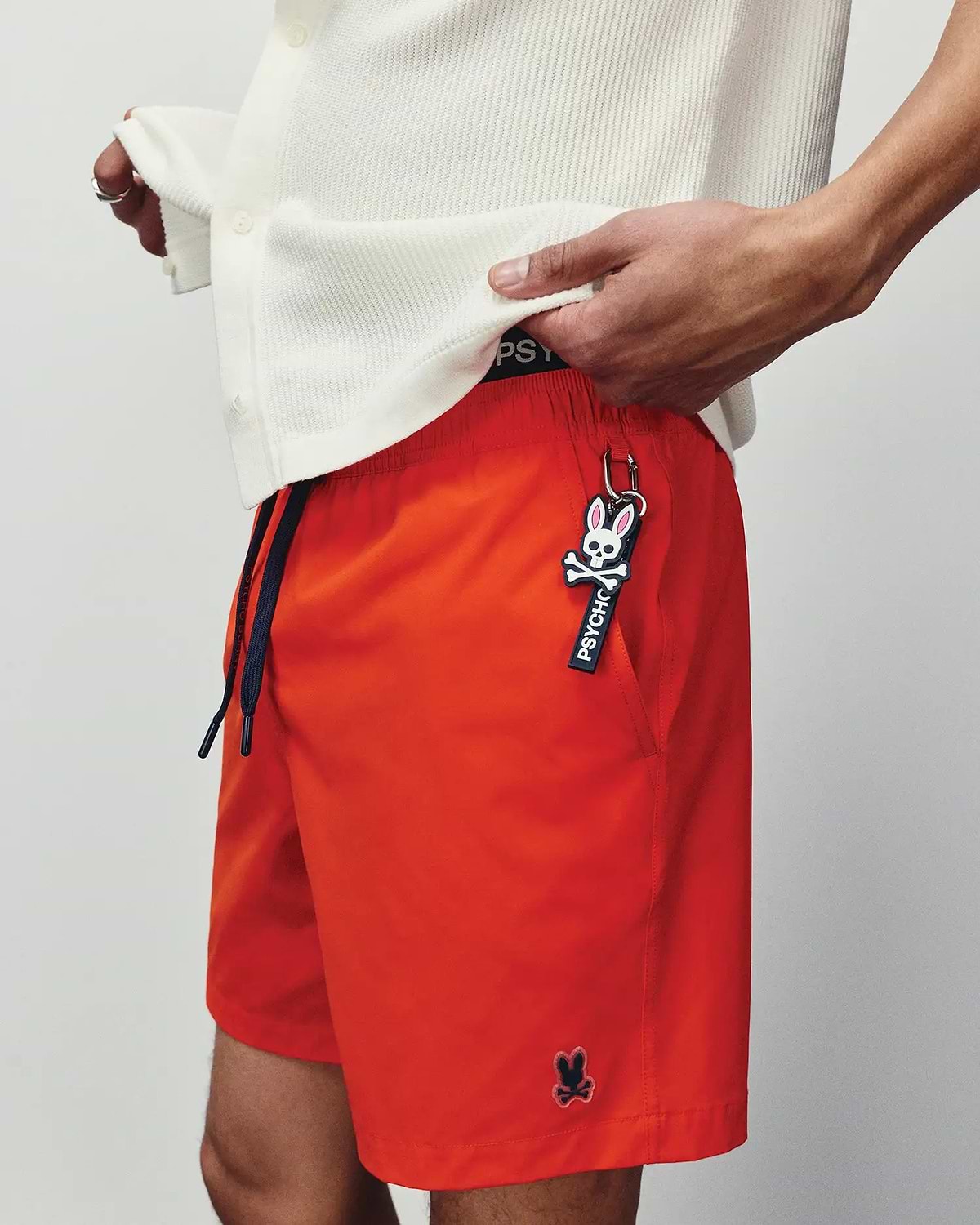 Mens Samos Hydrochromic Printed Swim Trunk in vibrant orange, with a relaxed fit, smooth quick-dry fabric, navy drawstring, black Psycho Bunny waistband, and a small embroidered black bunny skull logo.
