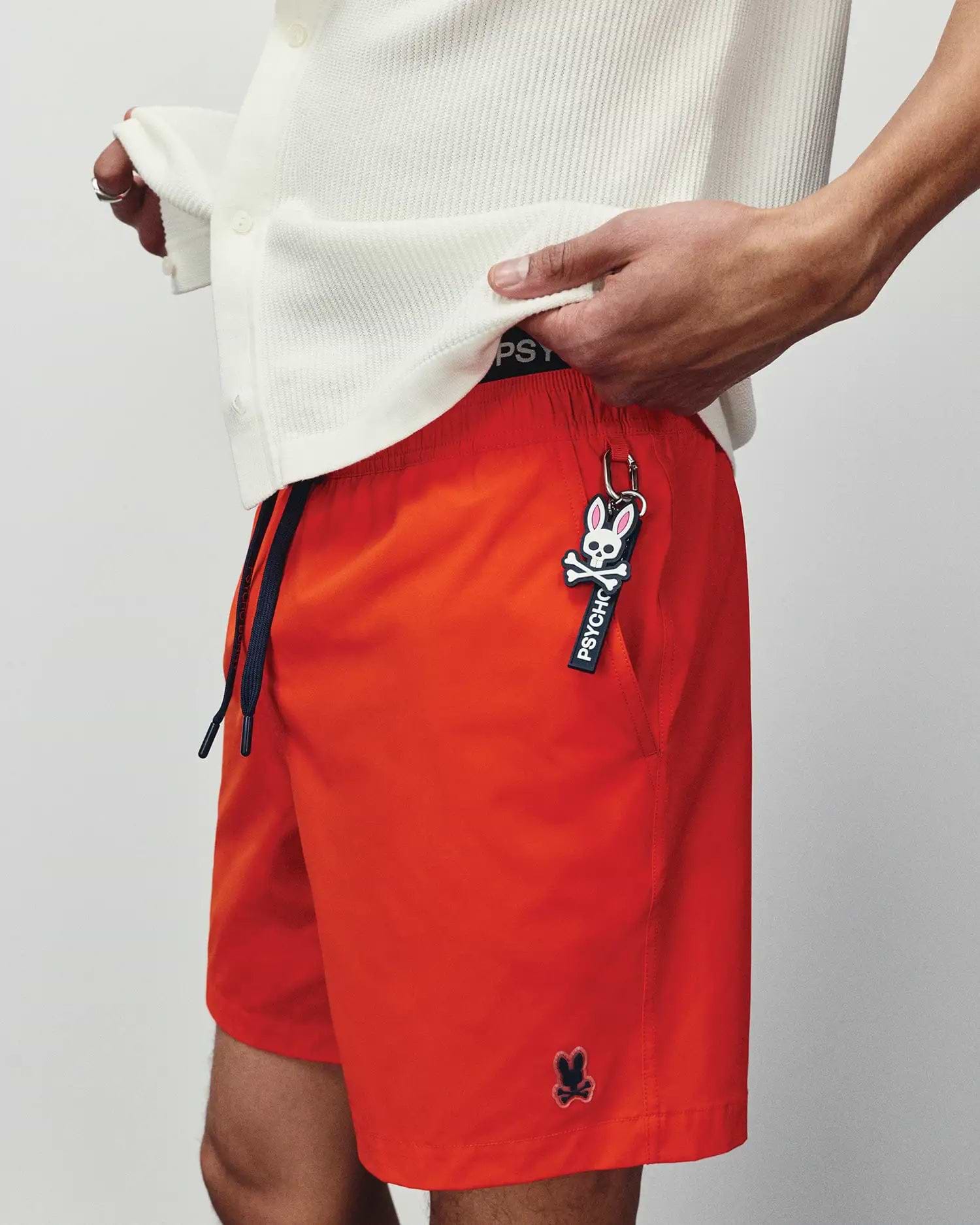Mens Samos Hydrochromic Printed Swim Trunk in vibrant orange, with a relaxed fit, smooth quick-dry fabric, navy drawstring, black Psycho Bunny waistband, and a small embroidered black bunny skull logo.
