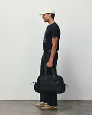 Black classic fit jersey t-shirt with a large white Psycho Bunny skull graphic, relaxed black pants, a cream cap, and a black Mens Nylon Duffle Bag featuring a subtle logo. (2)