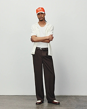 Mens Yann Knit Shirt: Relaxed fit, off-white ribbed knit short-sleeve collared shirt, layered over a white tee, with dark brown wide-leg trousers and an orange Psycho Bunny embroidered logo cap.