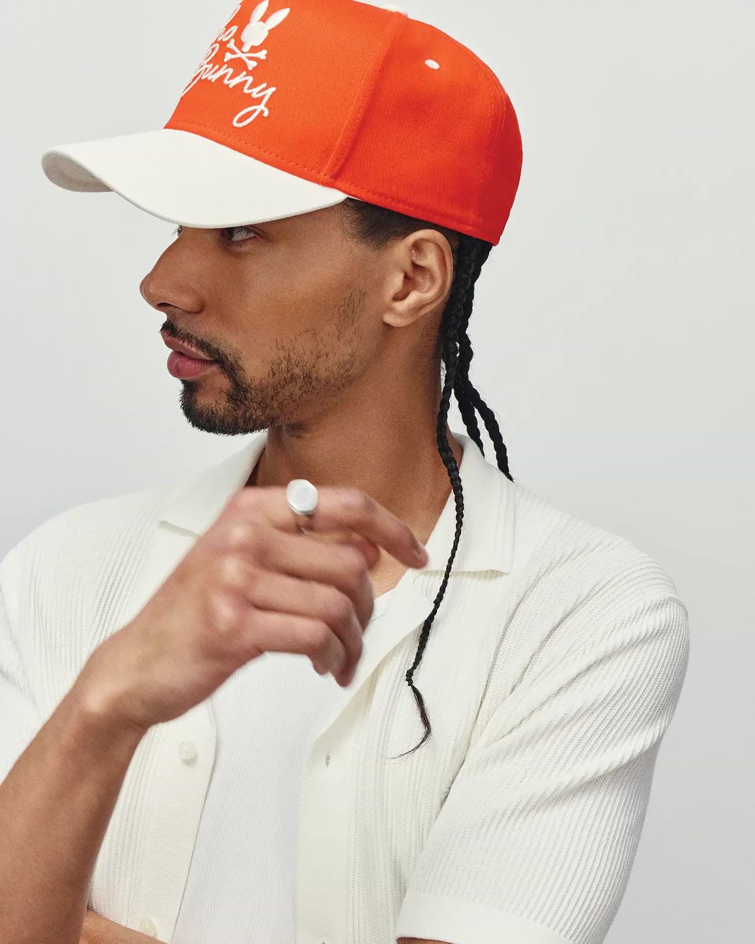 Mens Sable A-Frame Trucker Cap in orange with white brim and embroidered Psycho Bunny skull logo, paired with a white textured knit short-sleeve collared shirt.