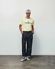 Mens Jaydon Wordmark Graphic Tee in pale yellow, a classic fit jersey knit t-shirt featuring a centered black script Psycho Bunny wordmark and iconic bunny skull logo with blue accents.