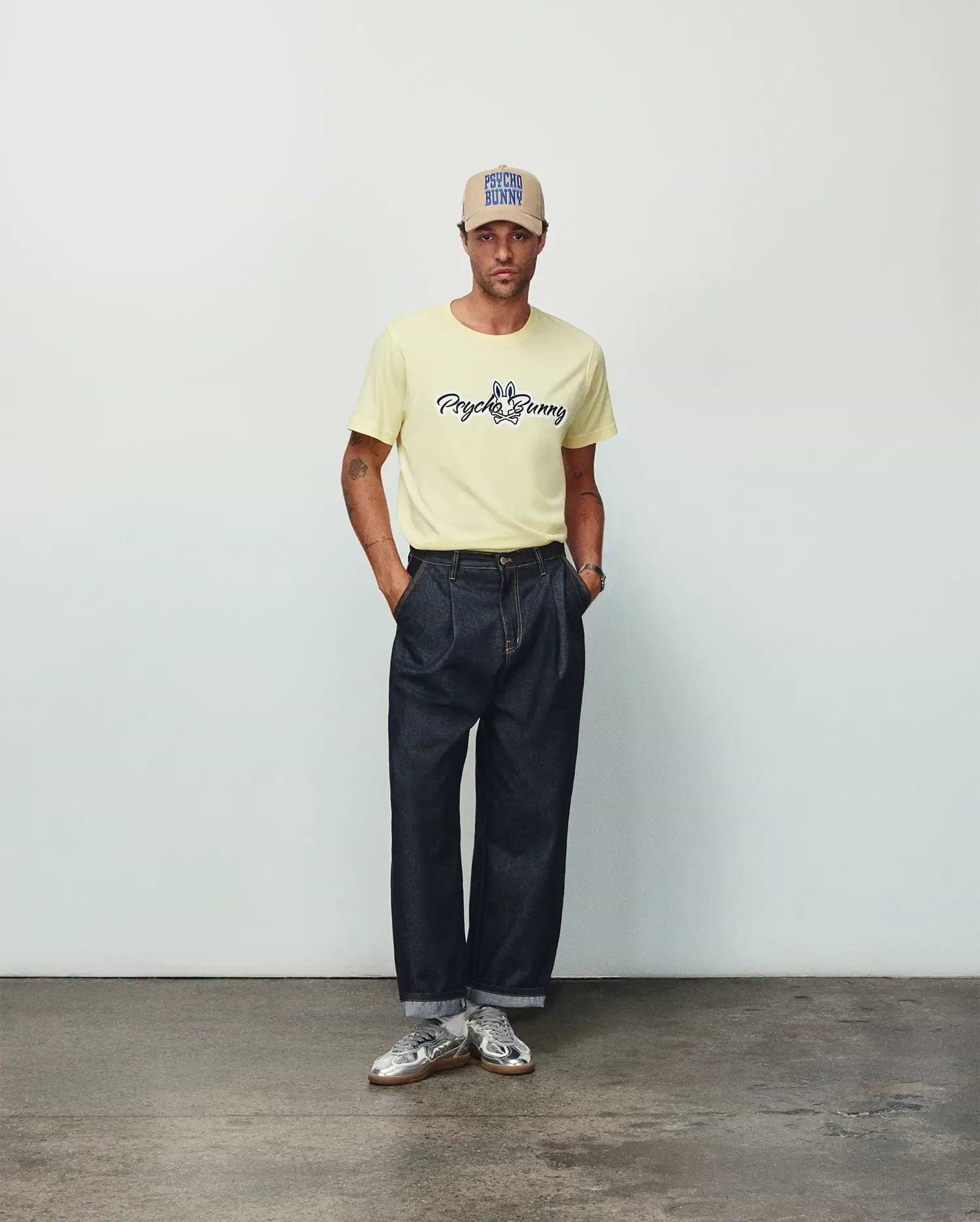 Mens Jaydon Wordmark Graphic Tee in pale yellow, a classic fit jersey knit t-shirt featuring a centered black script Psycho Bunny wordmark and iconic bunny skull logo with blue accents.