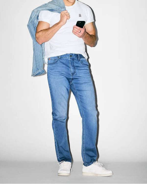 Premium white jersey t-shirt with small embroidered pink/black Psycho Bunny skull logo on chest, paired with slim-fit Mens Ace Knit Denim Pant in light blue, and a light wash denim jacket.