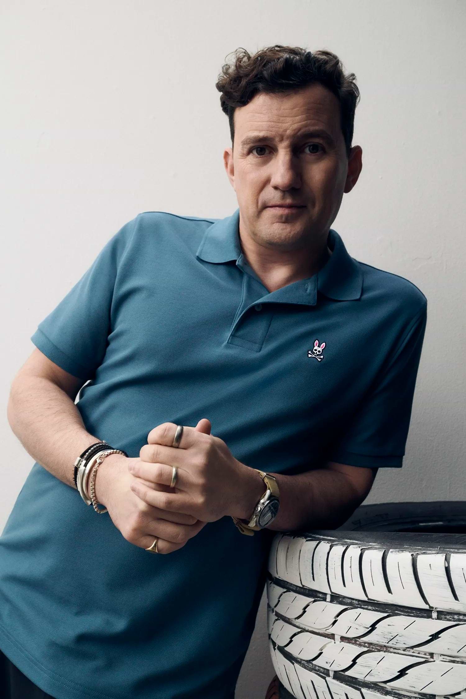 Mens Classic Pique Polo in teal blue, featuring a classic fit and visible pique knit texture. Small embroidered pink, white, and black Psycho Bunny skull logo on the left chest.