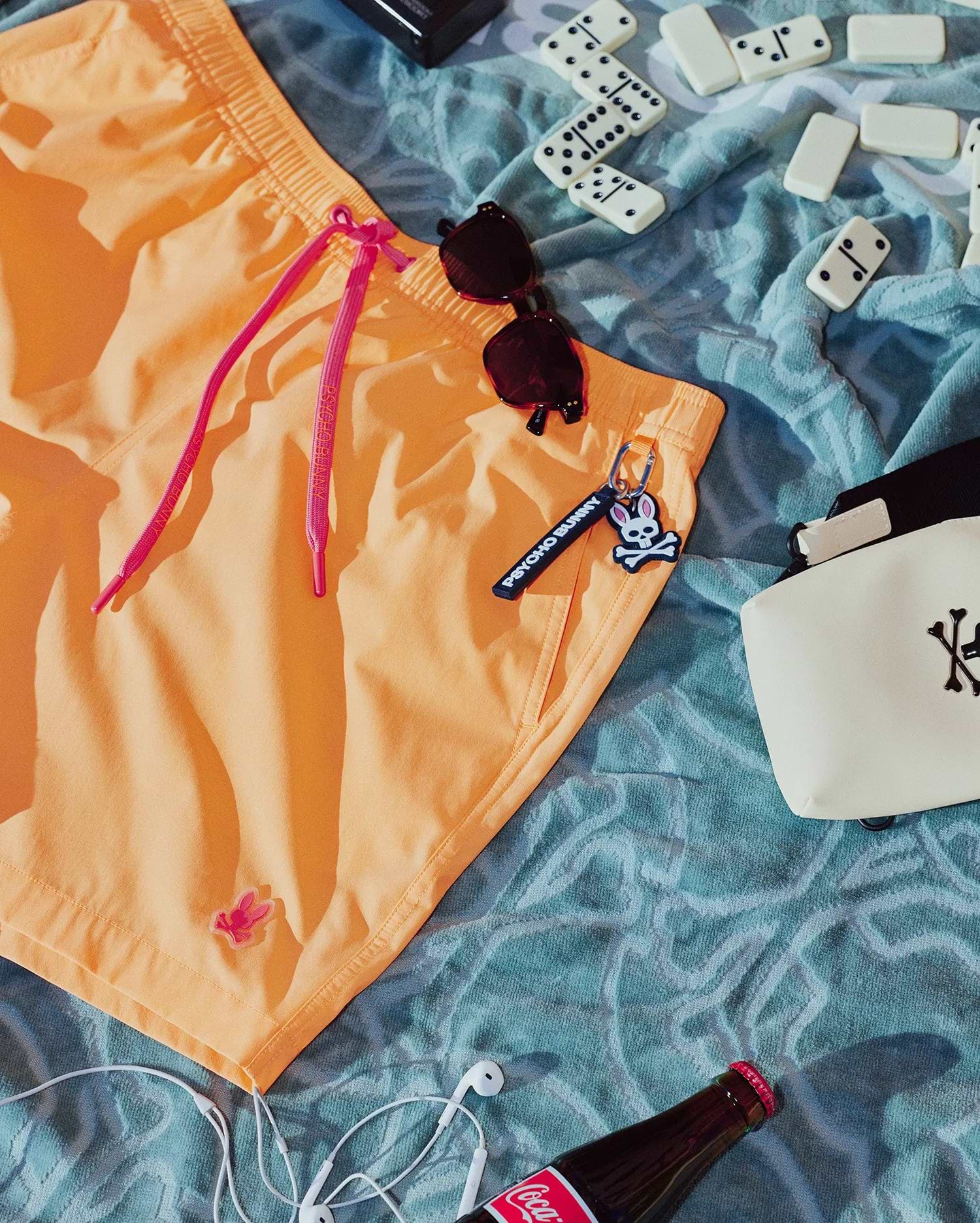 Mens Samos Hydrochromic Printed Swim Trunk in vibrant peach, featuring a relaxed fit, smooth quick-dry fabric, bright pink drawstrings with Psycho Bunny text, and a small pink bunny skull logo on the left leg.