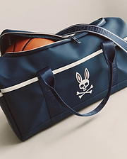 Classic Bunny Gym Bag in navy blue smooth fabric, featuring a prominent white and pink Psycho Bunny skull logo, white horizontal stripe, and branded navy strap with white text.